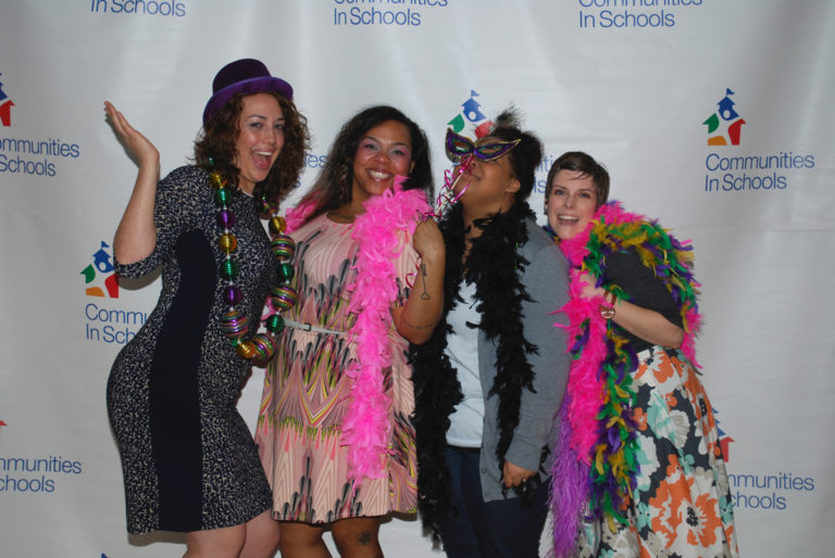 four ladies in mardi gras costume in front of Communities In Schools logo backdrop
