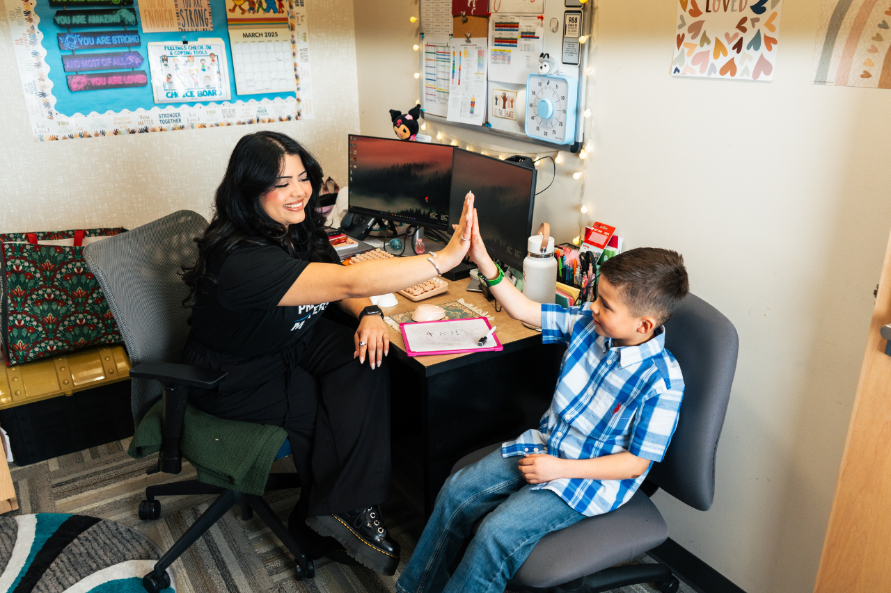 Photo of a Communities in Schools Site Coordinator high-fiving a student in a chair sitting next to her