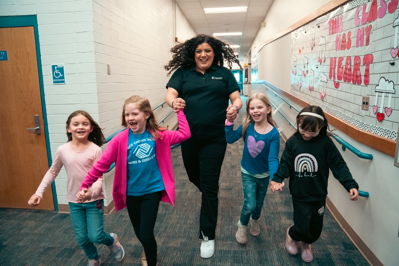 Site coordinator running down the hall, holding hands of elementary school students on both sides