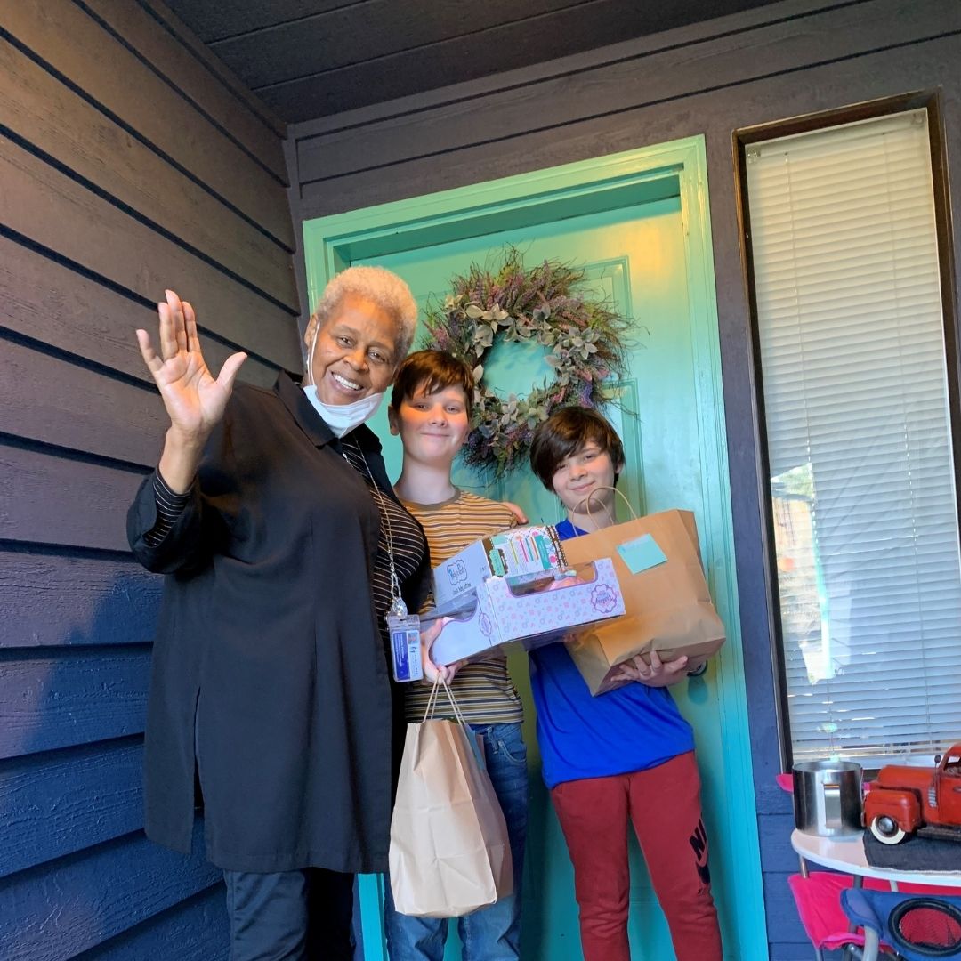 Pat with two smiling students at their door front.