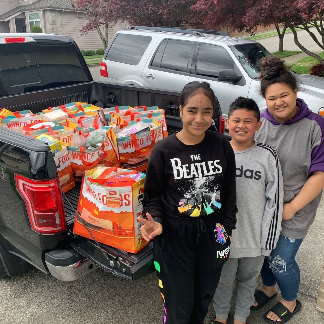 Students smiling next to a truck of grocery bags. 